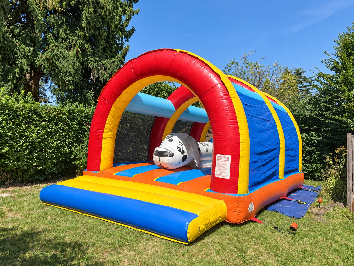 Gonflable rouge, bleu et jaune avec arches et décor ludique, installé dans un jardin